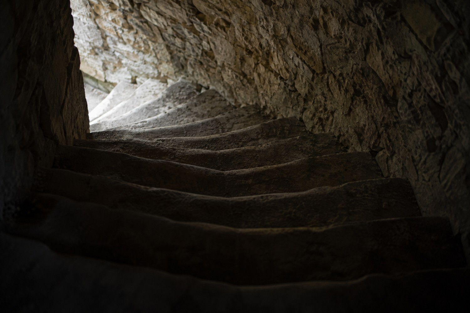 Un escalier de pierre en colimaçon montant vers la lumière, dans l'épaisseur d'un mur ancien.